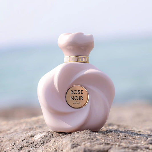 Pink 'Rose Noir' perfume bottle on a textured surface with a blurred natural background