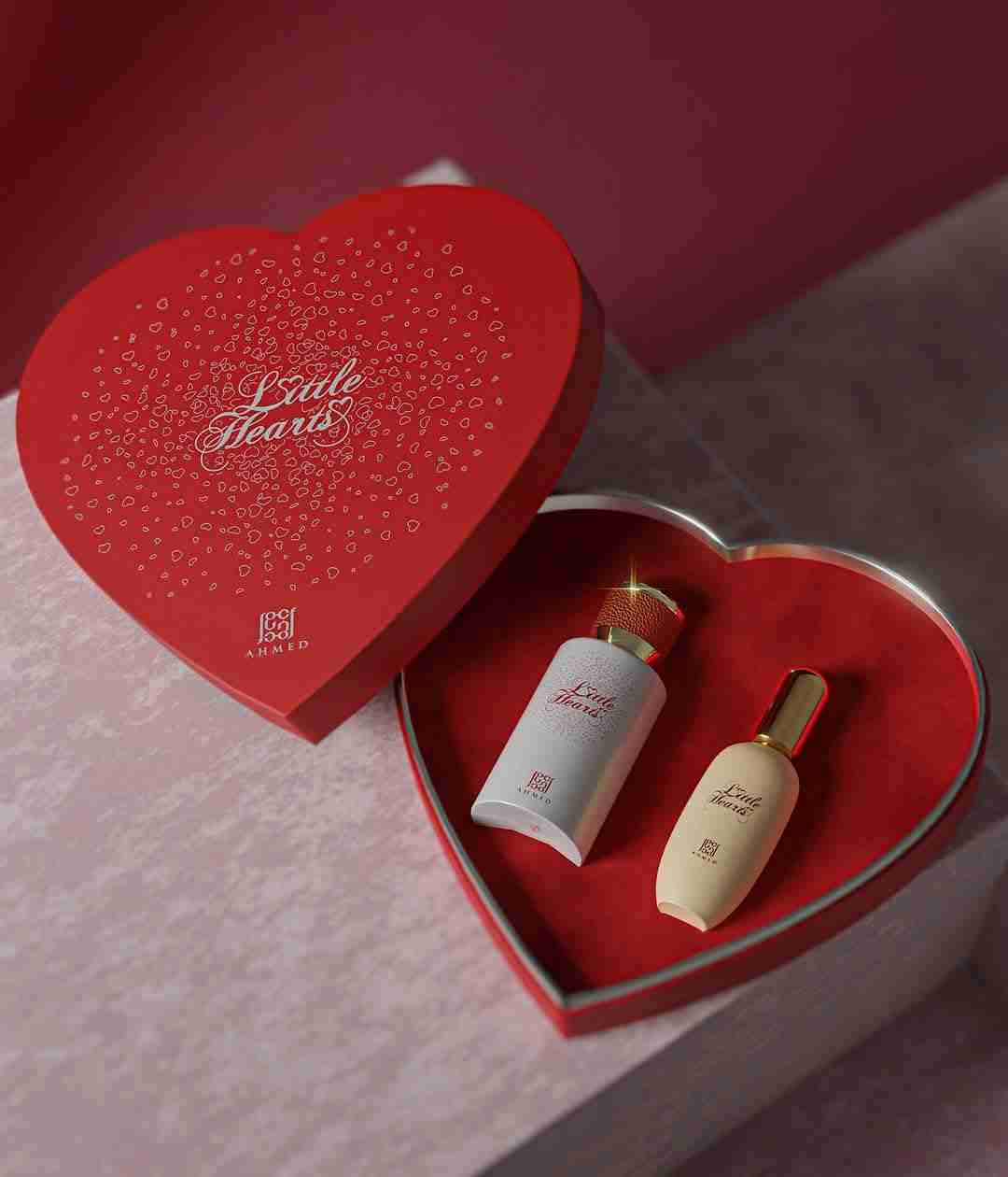 Red heart-shaped box with two small bottles inside on a pink background