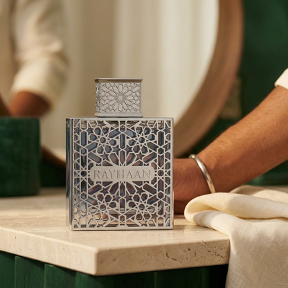 Rayhaan Aquatica 100ml perfume on an ivory vanity beside linen, with a person getting ready.