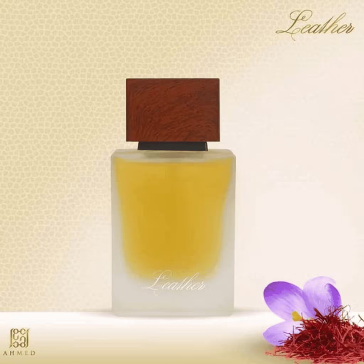 A frosted glass perfume bottle with a dark brown wood-grain cap, filled with amber-yellow liquid, labeled 'Leather'. The bottle is set against a textured beige background with a purple flower and red saffron in the lower right corner.