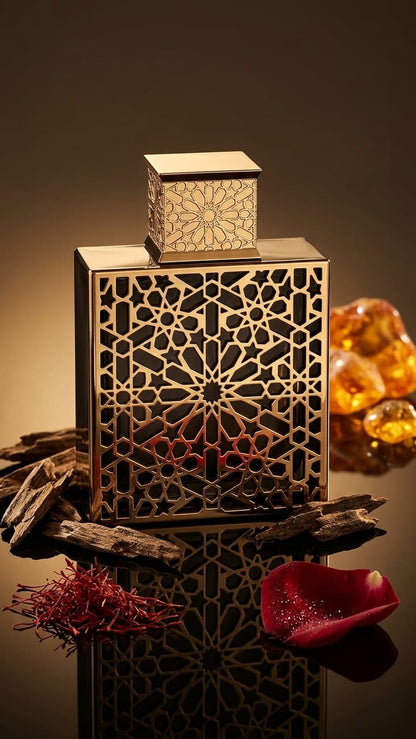 An ornate rectangular perfume bottle with intricate geometric cutout patterns on the front and cap, styled with amber resin, saffron threads, and a red rose petal on a reflective dark surface.