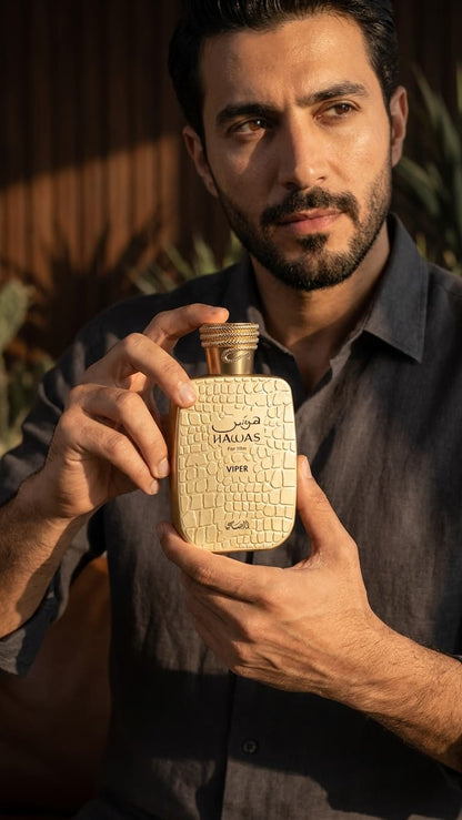 A man holds a textured beige perfume bottle labeled 'HABIB' and 'VIPER' against a warm, dark background.